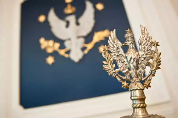 Godło Uniwersytetu czyli orzeł dawny polski w koronie, z rozpostartymi skrzydłami, trzymający w lewym szponie gałązkę palmową, a w prawym laurową, w koło w pięciokąt pięć gwiazd znaczących pięć akademicznych wydziałów. W tle obraz, na kórym jest godło UW